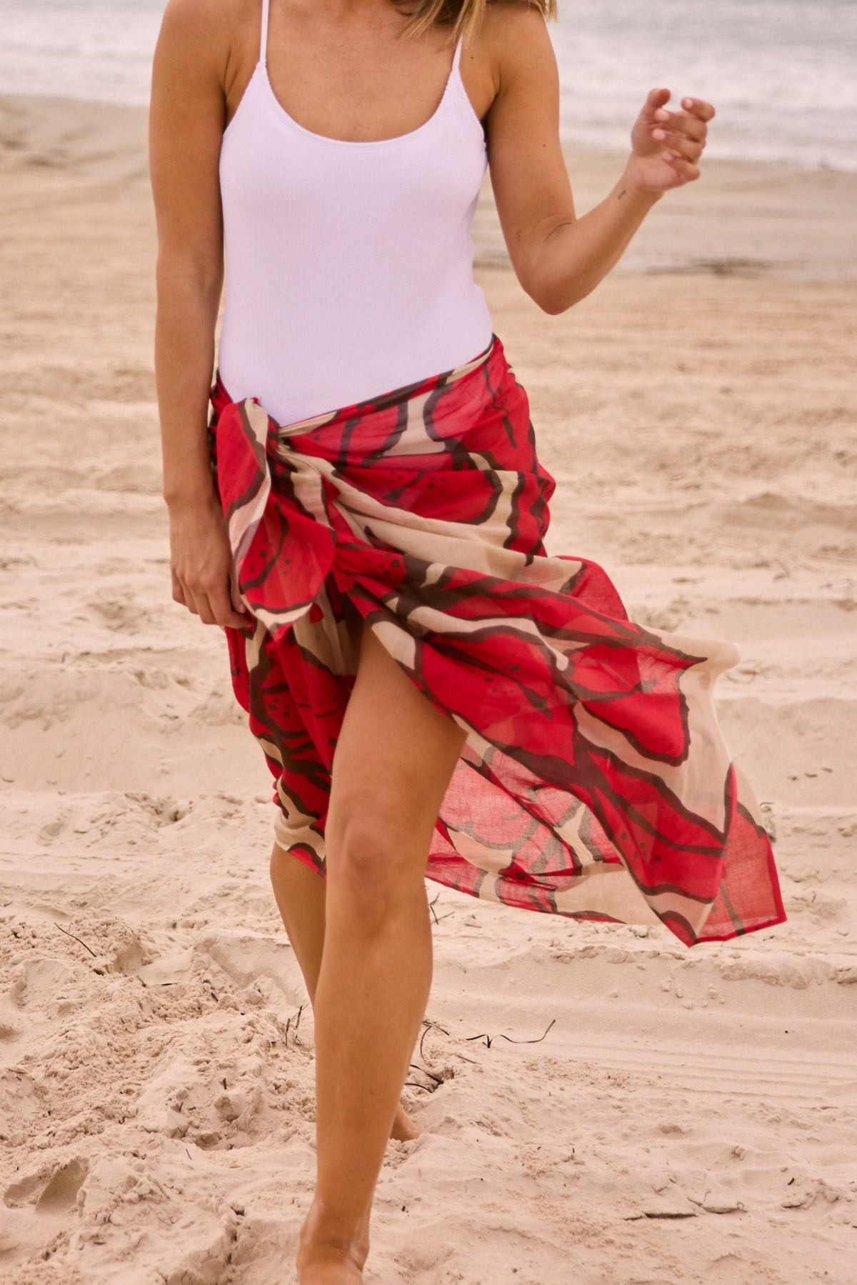 ELSHAM BOUTIQUE crimson floral cotton sarong worn by a woman on a sandy beach