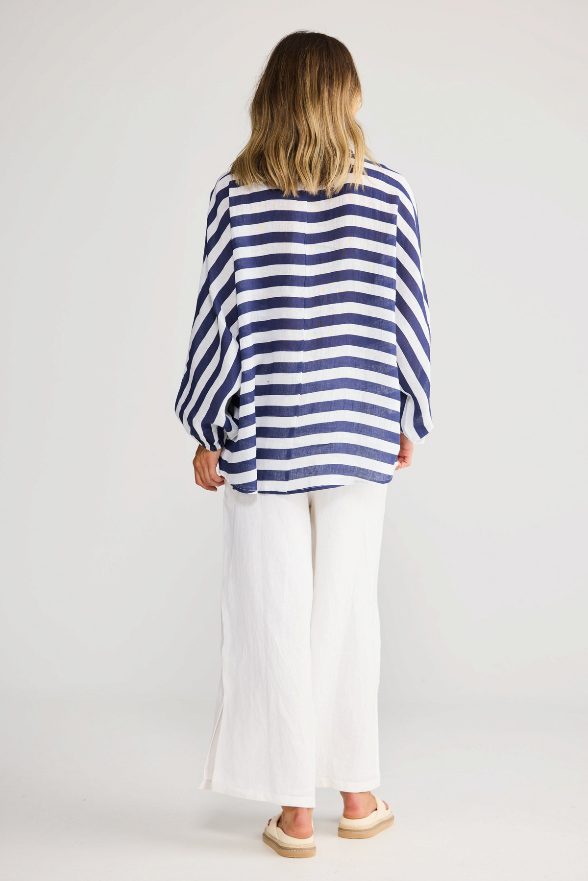 ELSHAM BOUTIQUE navy striped oversized linen shirt with exaggerated sleeves, worn with white trousers, back view.