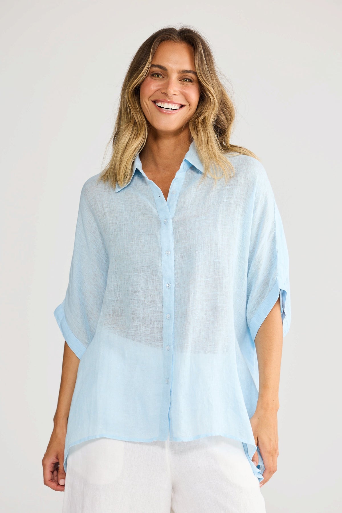 ELSHAM BOUTIQUE light blue oversized linen shirt with a collared neckline and short sleeves worn by a smiling woman.