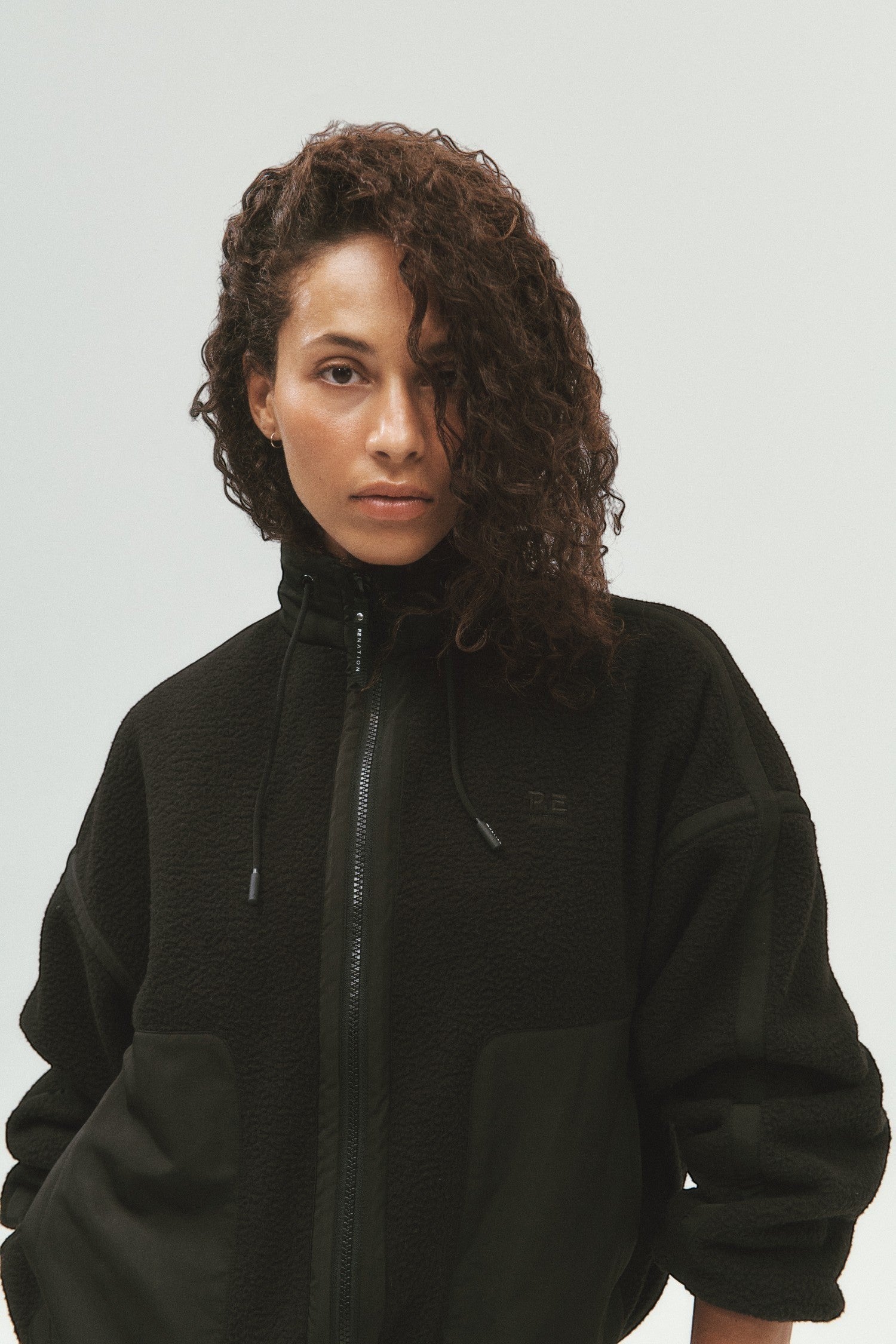 Model wearing ELSHAM BOUTIQUE black Lennon sherpa jacket with zip closure, contrast taping, and chest embroidery.