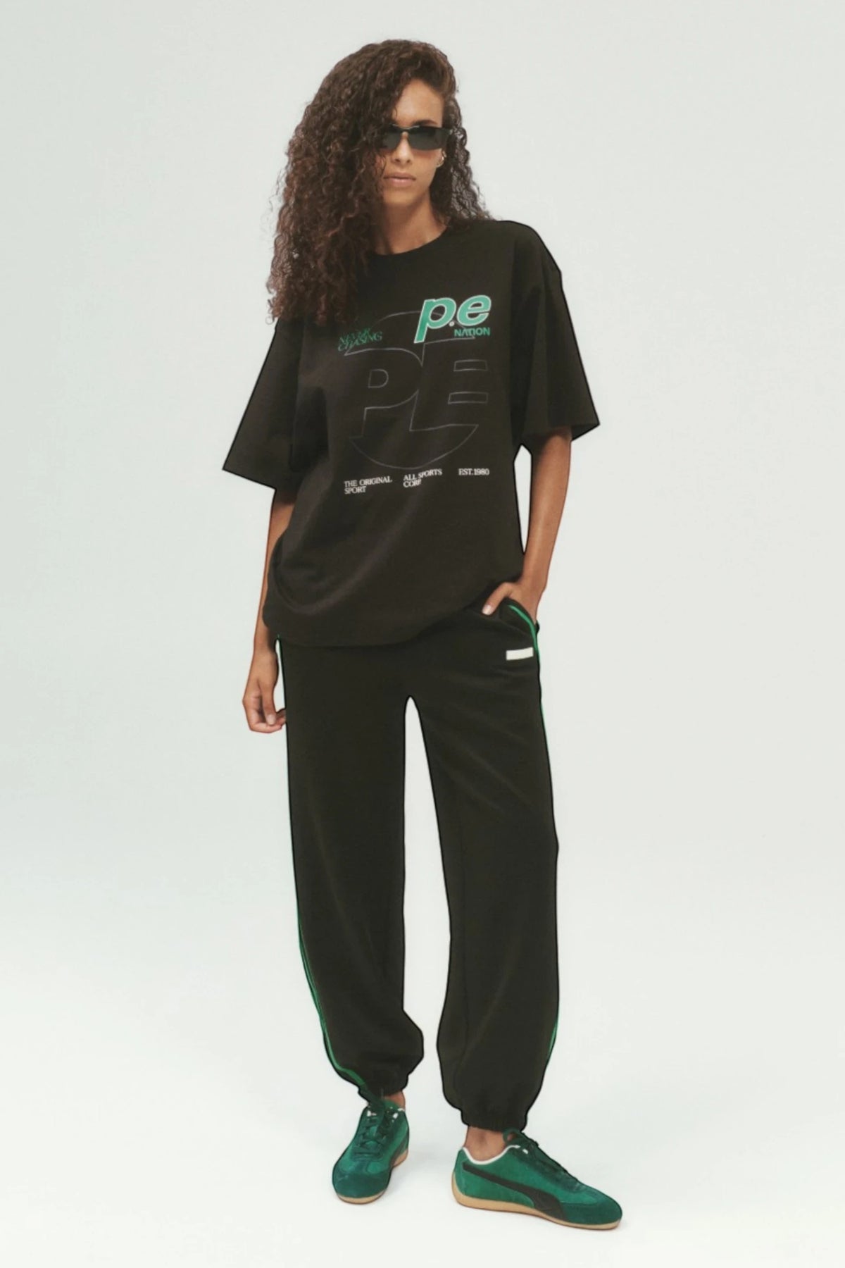 Model wearing ELSHAM BOUTIQUE black Clarity track pants with contrast side stripes and cuffed hems.
