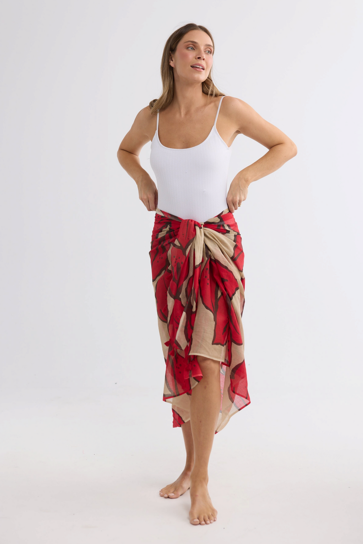 Model wearing an ELSHAM BOUTIQUE crimson floral cotton sarong over a white bodysuit against a white background