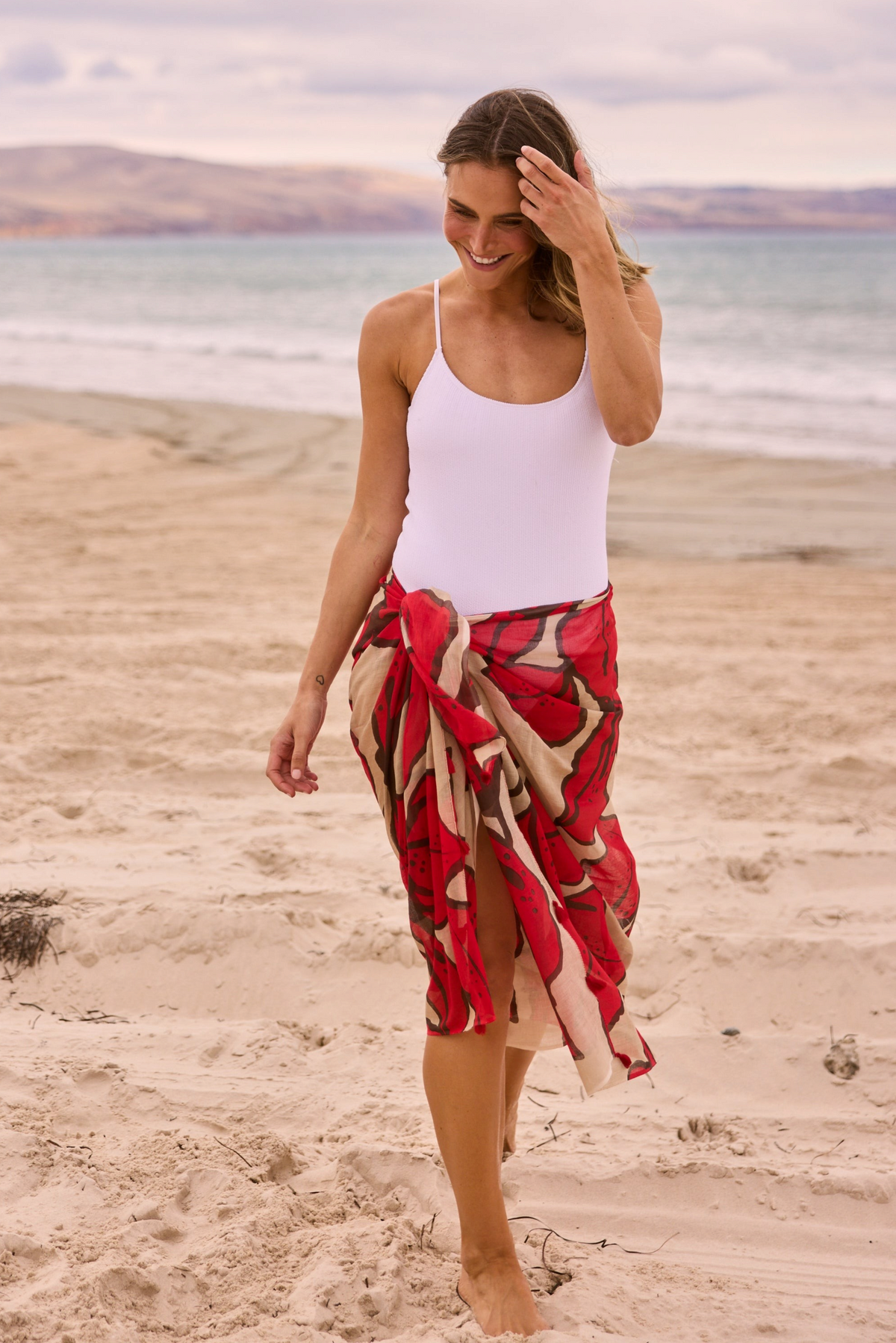 ELSHAM BOUTIQUE Stella sarong scarf in crimson floral print worn by a woman on a sandy beach