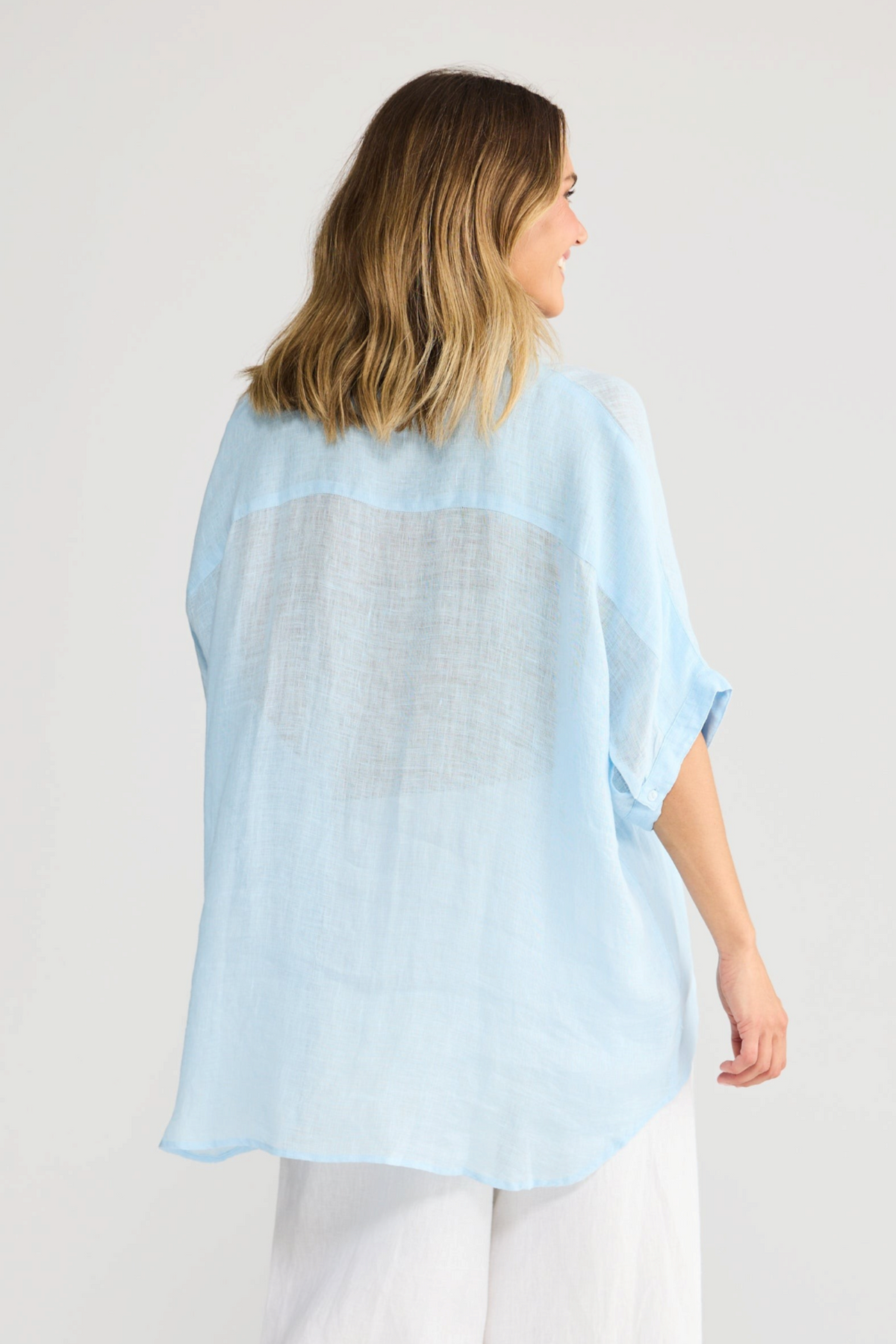 ELSHAM BOUTIQUE light blue linen oversized shirt with short sleeves, worn by a woman from the back view.