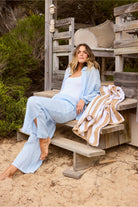 ELSHAM BOUTIQUE light blue linen shirt worn by a woman sitting on wooden steps in a relaxed, oversized fit.