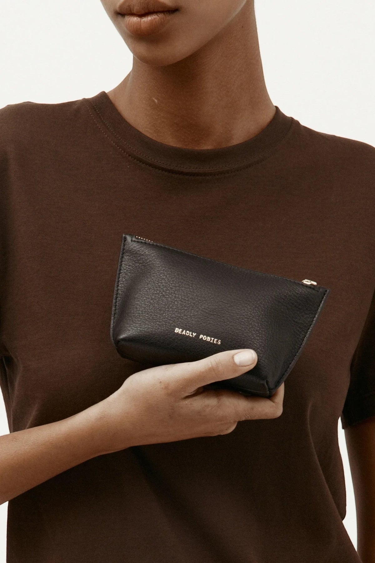 ELSHAM BOUTIQUE black calf nappa leather mini pouch with brass zip closure and gold foil logo held in hand