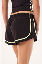 Back view of ELSHAM BOUTIQUE black athletic shorts with soft yellow piping and side zipper pocket