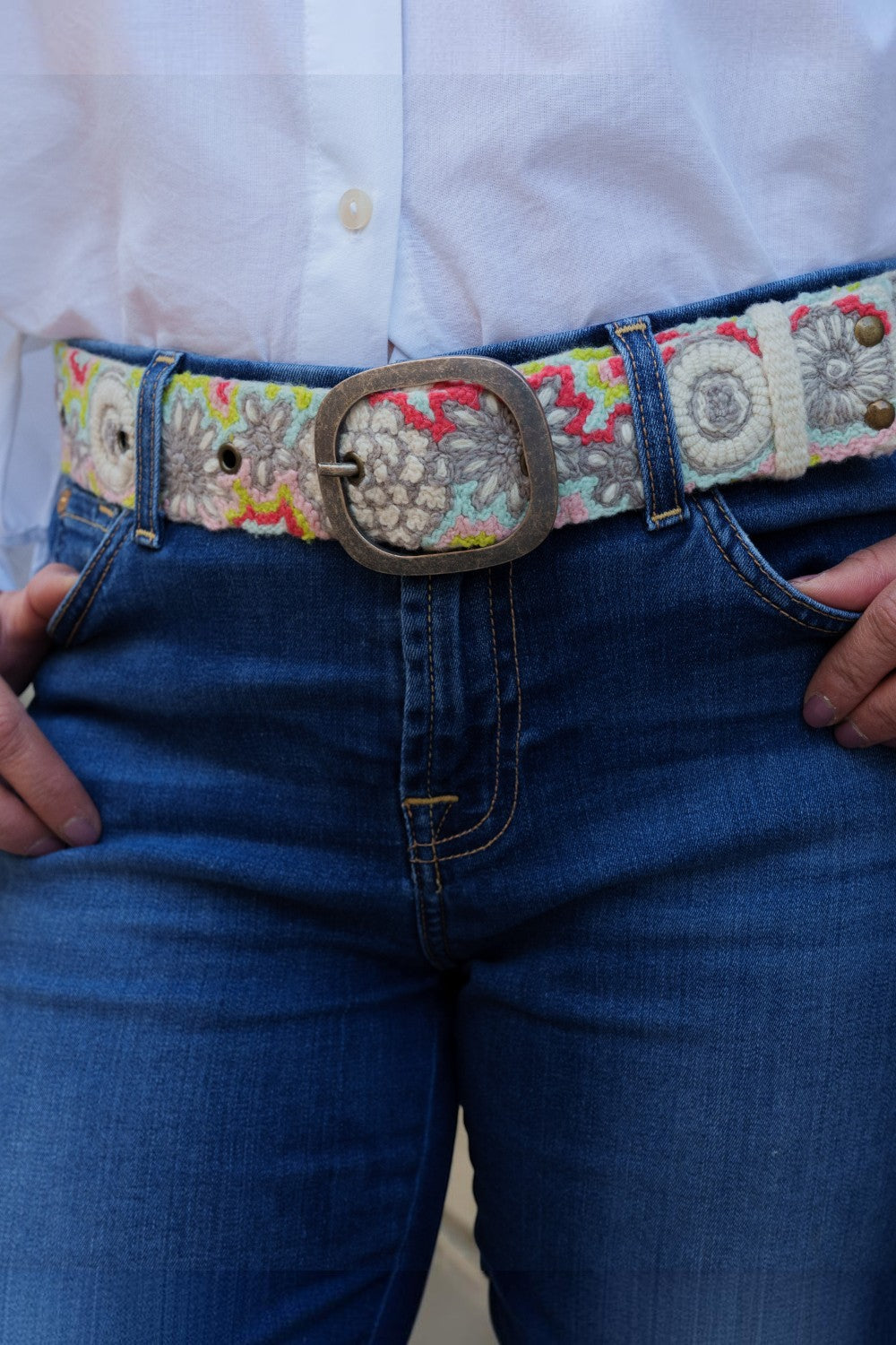 ELSHAM BOUTIQUE wool belt with colorful floral embroidery and a vintage-style metal buckle worn over blue jeans.