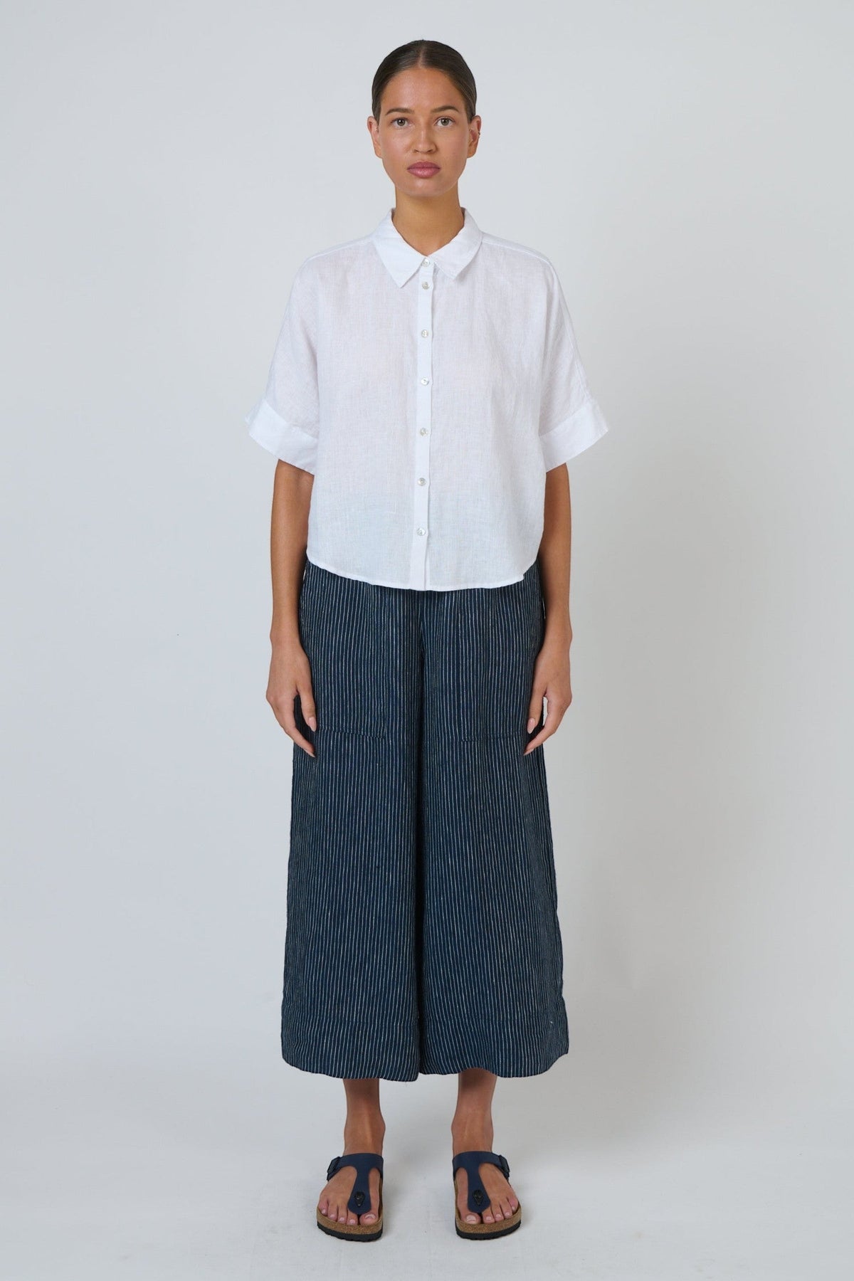 Model wearing ELSHAM BOUTIQUE navy pinstripe linen wide-leg cropped pants with oversized front pockets