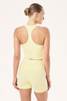 ELSHAM BOUTIQUE soft yellow ribbed racerback tank top with internal shelf bra worn by a model from the back view